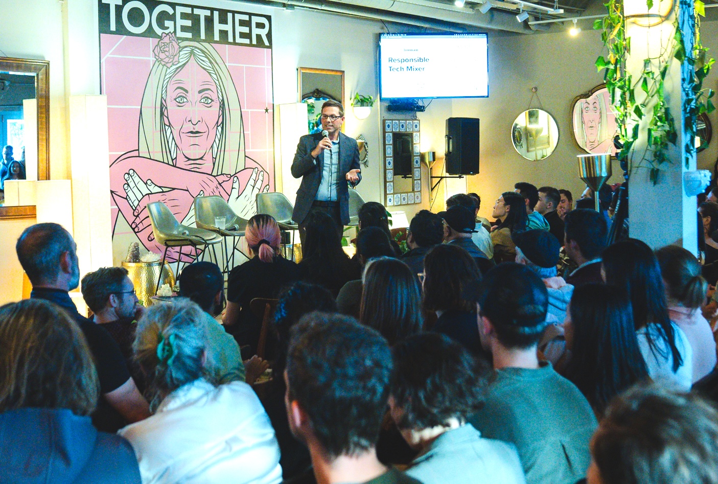 A man speaking to a group; a poster behind him is titled TOGETHER and a slide reads Responsible Tech Mixer